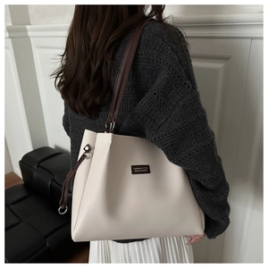 Dettaglio di una grande borsa tote crema con targhetta in pelle e tracolle marrone scuro