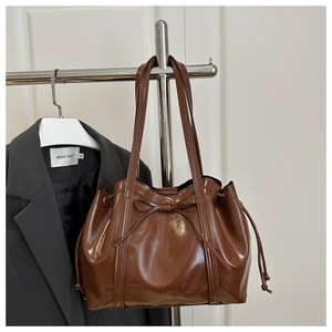 Detail of a brown patent leather tote bag with bow accent and side drawstring design