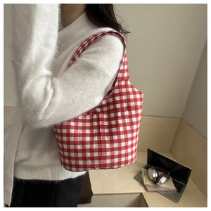 Close-up of red gingham bucket bag worn with a white cardigan in a cozy indoor setting