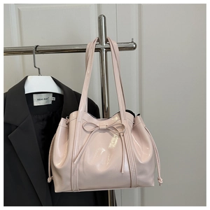Detail of light pink patent leather tote bag featuring ribbon bow and drawstring sides