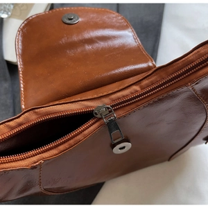 Detailed close-up of brown faux leather saddle bag with zipper and magnetic metal buckle