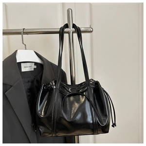 Close-up of black glossy patent leather tote bag featuring a bow and drawstring details