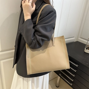 Minimalist beige tote bag in pebbled leather with stitched dots shown on shoulder
