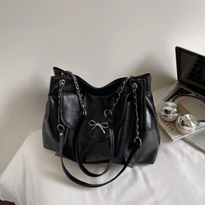 Détail du sac cabas noir brillant avec nœud argenté et bandoulière en chaîne sur bureau