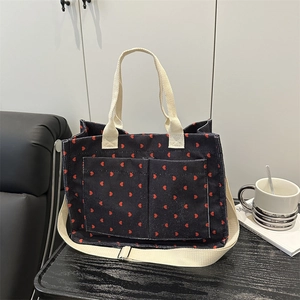 Black corduroy tote bag with red heart pattern, dual pockets, and adjustable strap