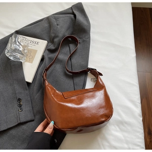 Close-up of brown PU leather saddle bag with adjustable strap on a gray blazer background