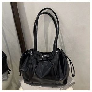 Detail of glossy black patent leather tote bag featuring a bow and drawstring design