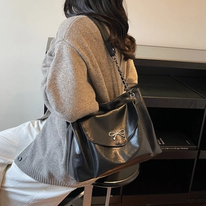 Gros plan du sac cabas en cuir noir brillant avec boucle nœud argenté et chaîne