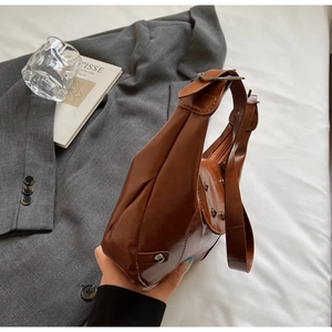 Detail of caramel brown saddle bag with metal studs and glossy finish in urban setting