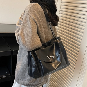 Gros plan d'un sac cabas en cuir verni noir avec nœud argenté et bandoulière en chaîne