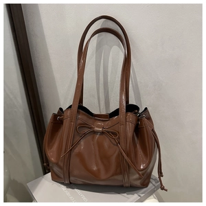 Detail of glossy brown leather tote with bow decoration and drawstring structure