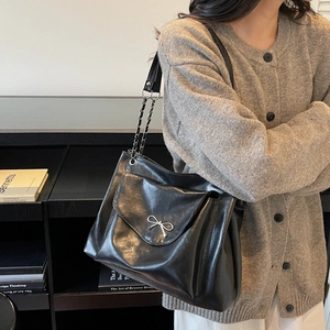 Détail du sac cabas noir brillant avec un nœud argenté et une bandoulière en chaîne métal
