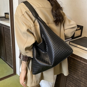 Détail d'un grand sac hobo tressé noir porté par un mannequin dans un cadre intérieur
