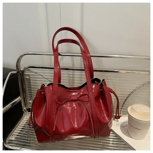 Detail of red patent leather tote bag featuring a decorative bow and drawstring closure