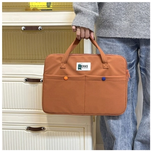 Détail de la housse d'ordinateur orange caramel avec étiquette blanche et boutons décoratifs