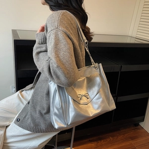 Détail d'un grand sac fourre-tout argenté avec nœud métallique et bandoulière en chaîne
