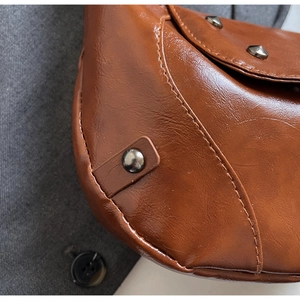 Detail of vintage brown leather saddle bag with bronze rivets and textured stitching