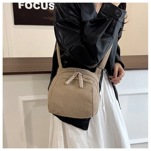 Detail of khaki corduroy crossbody bag featuring a textured weave rope zipper pull on a model