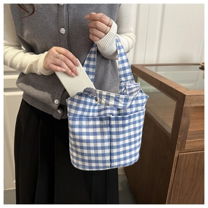 Detail showing blue and white checkered canvas bucket bag with functional front pockets
