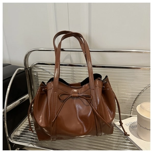 Detailed view of brown glossy tote bag with bow detail on a minimalist shelf