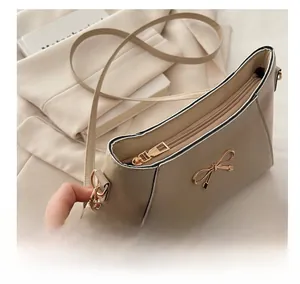 Close-up of smooth gold zipper and bow detail on light brown faux leather shoulder bag