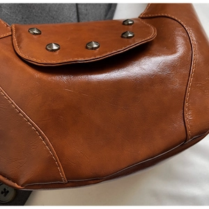Detailed close-up of brown vintage saddle bag featuring metallic cone studs and premium texture