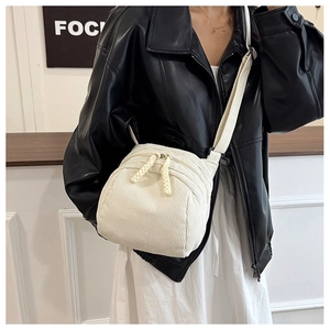 Detail of white corduroy crossbody bag with woven zipper pulls worn by model