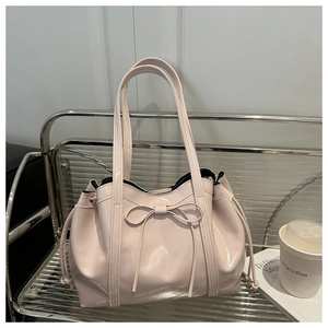 Close-up of pink patent leather tote bag featuring a decorative bow and drawstring detail