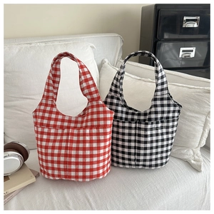 Close-up of red and black gingham canvas bucket bags with front pockets on a white sofa
