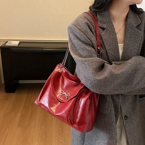 Détail d'un cabas en cuir verni rouge avec nœud argenté porté par un mannequin femme