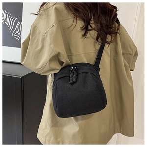 Detailed close-up of black pleated corduroy shell bag with textured fabric and woven zippers