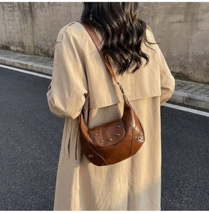 Brown retro saddle bag with metallic rivets worn over a beige trench coat outdoors