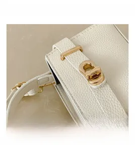 Detailansicht des goldenen Metalldrehverschlusses an der weißen Lederhandtasche mit Narbenprägung