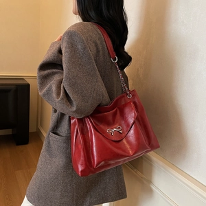 Détail d'un sac cabas bordeaux brillant avec nœud argenté et bandoulière chaîne