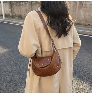 Brown vintage saddle bag with rivet details worn over a beige coat in street setting