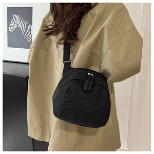 Detail of black corduroy shell bag featuring a woven zipper and adjustable shoulder strap