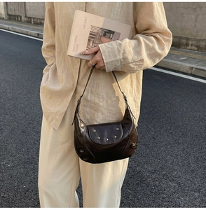Detail of dark brown crescent saddle bag with metallic studs and glossy leather finish