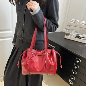 Red patent leather tote bag with bow detail and drawstring shown in a lifestyle setting