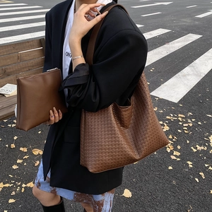 Détail d'un sac hobo tressé marron foncé et d'une pochette zippée assortie dans la rue