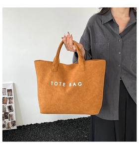 Nahaufnahme der karamellfarbenen Wildleder-Tragetasche mit weißem TOTE BAG-Schriftzug