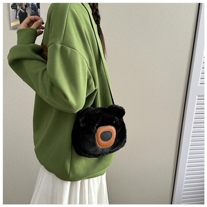 Detail of the cute black plush bear crossbody bag worn over a casual green sweater