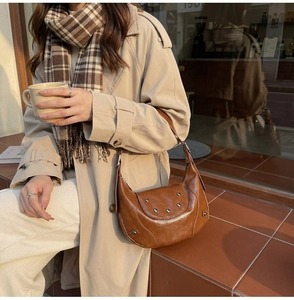 Close-up of brown vintage hobo bag with silver rivets on rustic brick background