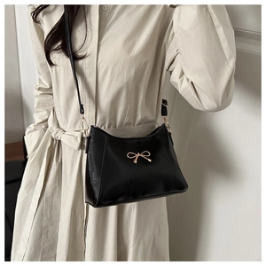 Close-up of glossy black shoulder bag featuring a refined golden butterfly metal clasp