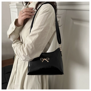 Detail of a black glossy patent leather hobo shoulder bag with a gold butterfly buckle