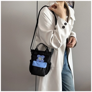 Detail view of black canvas crossbody tote with blue zip pocket and pixelated M patch