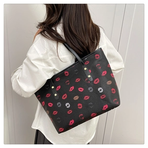 Detail shot of black tote bag with red lip print and golden hardware rivets on textured leather