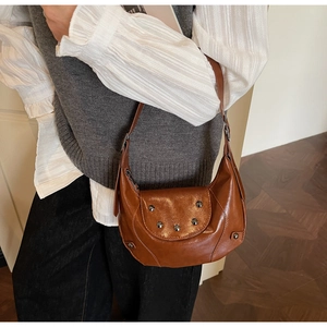 Detail of vintage brown leather saddle bag featuring glossy pleated texture and silver rivets
