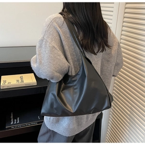 Detailed side view of a large black matte leather tote bag worn over the shoulder