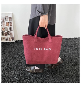 Dunkelrote Tragetasche aus Wildleder mit weißem TOTE BAG-Aufdruck, gehalten von einem Modell