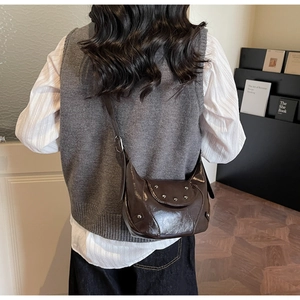 Detail of dark brown polished leather saddle bag with silver studs on shoulder model